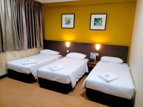 three beds in a room with yellow walls at YMCA Kuala Lumpur in Kuala Lumpur