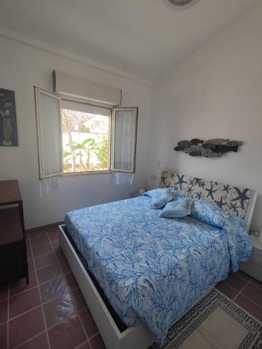 a bedroom with a bed with a blue comforter and a window at Oasi Villa Giusy in Capoterra