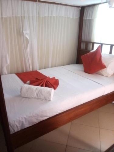 a bed with white sheets and red pillows on it at sunset suswa apartment in Mombasa