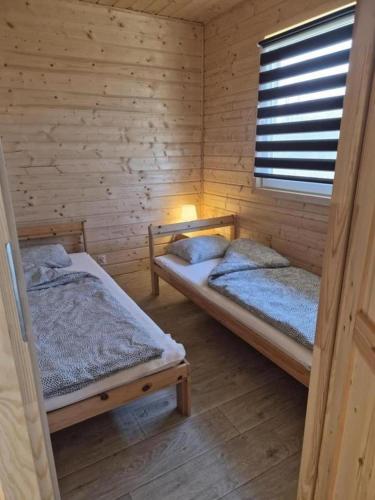 two beds in a wooden room with a window at Domki Letniskowe U Żuni in Chłopy