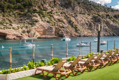 a row of chairs sitting next to a body of water with boats at Palladium Hotel Cala Llonga - Adults Only in Cala Llonga