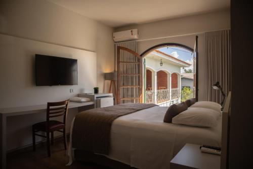 a bedroom with a bed and a desk and a window at Dom Ravello in Telêmaco Borba