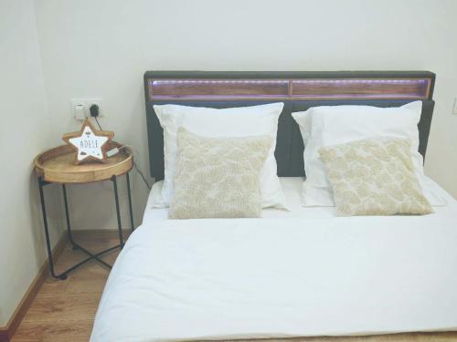a bed with white sheets and pillows next to a table at Chez Alice 2 in Montbéliard