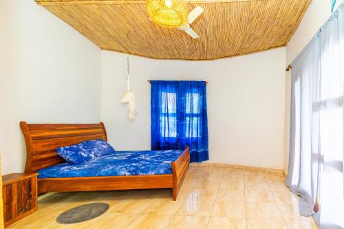 a bedroom with a bed with blue sheets and a ceiling at Tanema Creek in Brufut