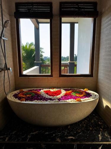 a bathtub covered in flowers in a bathroom with two windows at Villa Silas Ubud Bali in Ubud