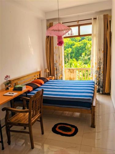 a bedroom with a bed and a table and a window at Papa's Resort Dunhinda in Hinnarangahakumbura