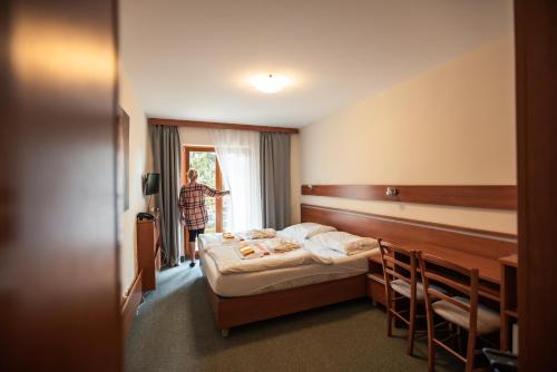 a hotel room with a bed and a person looking out the window at Hotel Jantar Dudince in Dudince