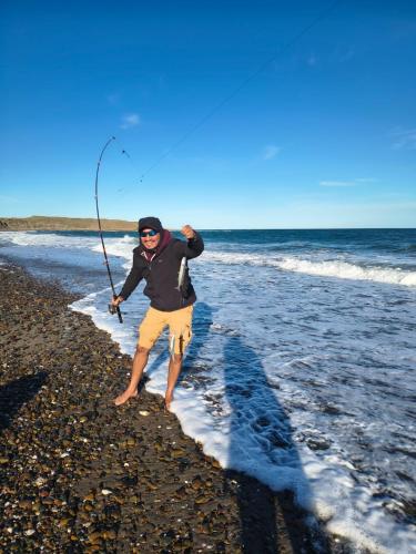 a man standing on the beach with a fishing rod at Arena & mar in Las Grutas
