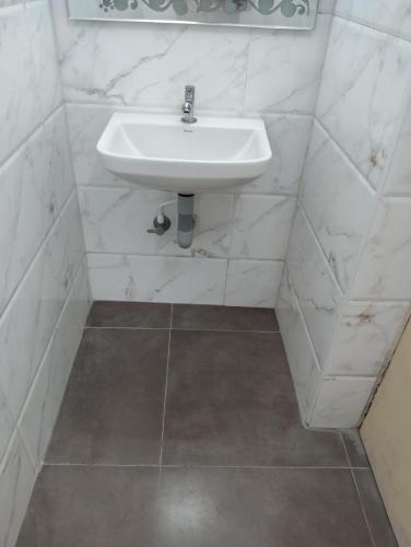 a white sink in a white tiled bathroom at Hotel ESS Paradise in Coimbatore