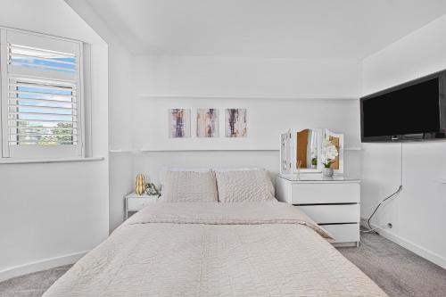 a white bedroom with a bed and a flat screen tv at 2 Bed Flat 10mins Heathrow 1 Parking EV in Hanworth
