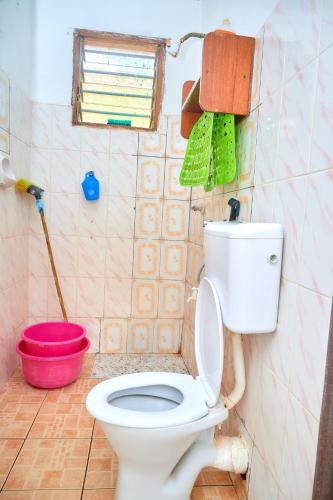 a bathroom with a toilet and a red bucket at Tranquil Terrace Cottages Diani in Diani Beach
