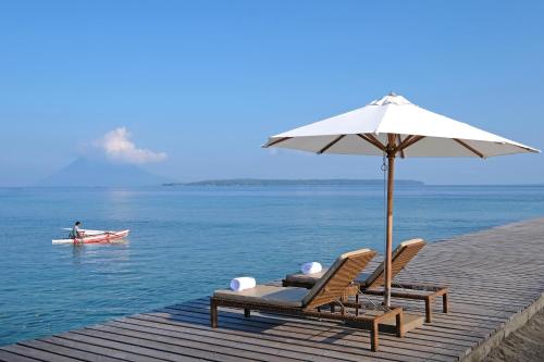 two chairs with an umbrella and a boat in the water at Grand Luley Manado in Manado