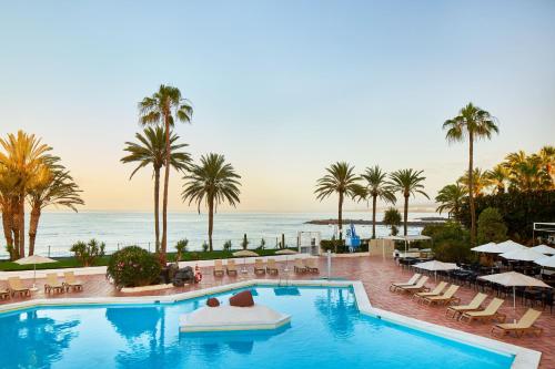 a swimming pool with palm trees and the ocean at SOL by Meliá Tenerife in Playa de las Americas