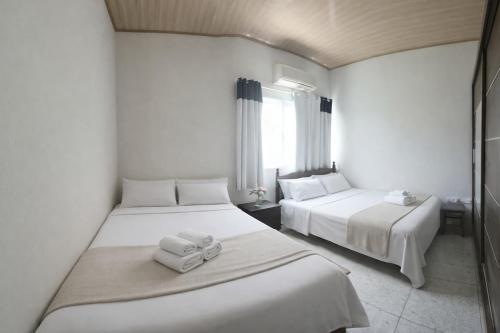 two beds in a white room with towels on them at Quarto privativo em Guriri casa de praia in São Mateus