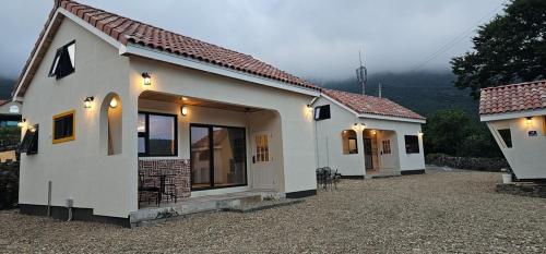 a small white house with a mountain in the background at Dara House Private Pension in Jangheung