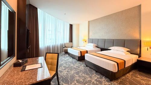 a hotel room with two beds and a desk at Grand Paragon Hotel Johor Bahru in Johor Bahru