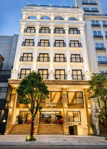 a large white building with a tree in front of it at Wilque Hotel Hanoi in Hanoi