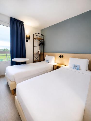 two beds in a hotel room with a window at Kyriad Hôtel La Fleche in La Flèche