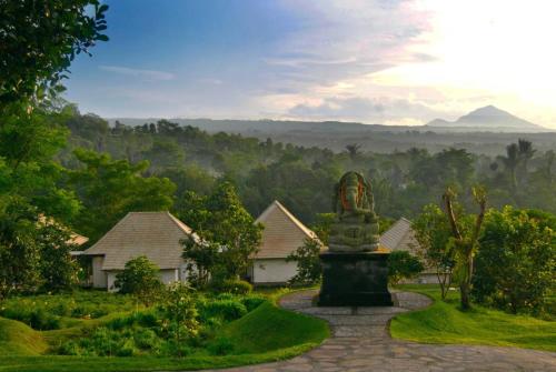 a statue in front of a house with mountains in the background at Moksha Wellness Bali in Plaga