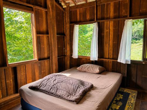 a bed in a wooden room with two windows at Indigo Homestay in Ban Huai Pong