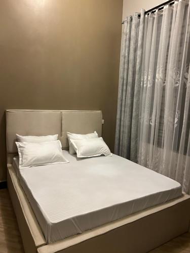 a bed with white sheets and pillows next to a window at Vn mbeya apartment in Mbeya
