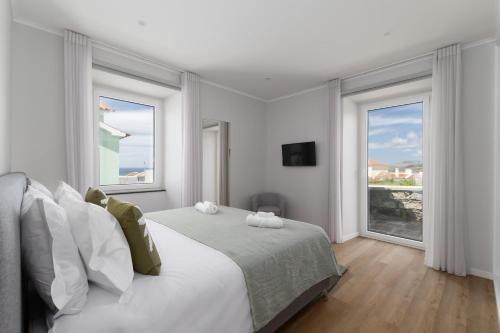 a white bedroom with a bed and two windows at Casa da eira in Ribeira Grande