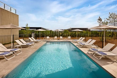 a swimming pool with chairs and umbrellas at Courtyard by Marriott Lyon Eurexpo Stadium in Genas