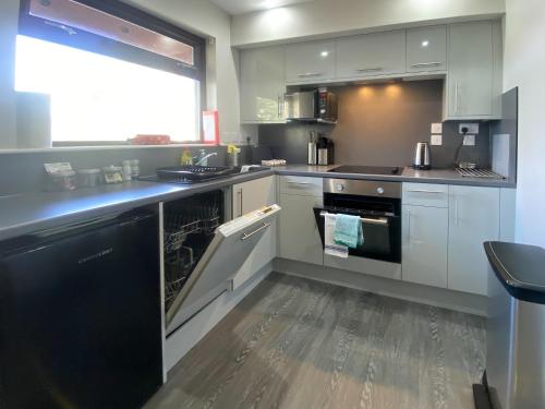 a kitchen with white cabinets and a black dishwasher at Puffin - Dubh Segir in Lerags