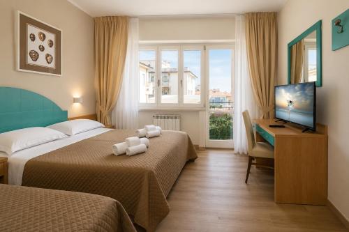 a hotel room with two beds and a desk and a television at Hotel Stella D'Italia in Viareggio