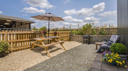 a patio with a wooden table and an umbrella at Roe Barn in Sherston