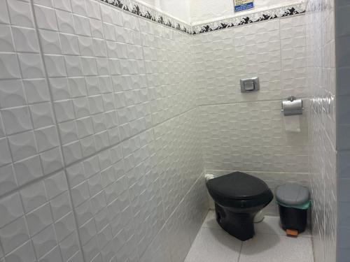 a bathroom with a black toilet in a white tiled wall at Hospedagem da Néli in Aparecida