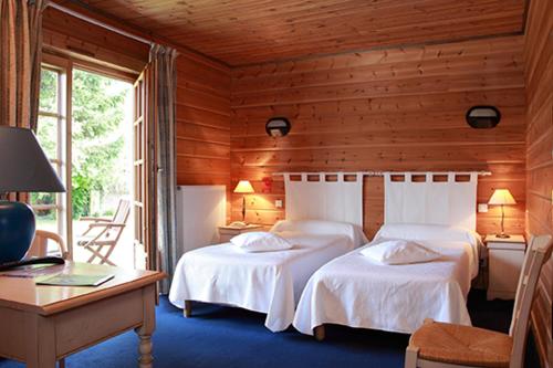 a bedroom with two beds and a desk and a window at Logis - Hôtel & restaurant Les Trois Fontaines in Marconne