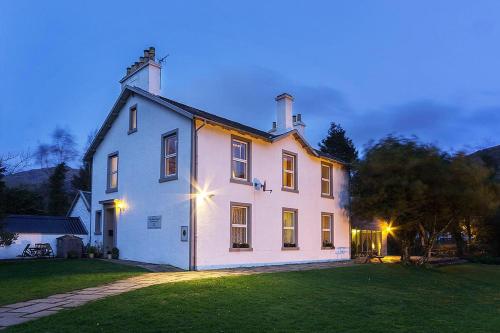 una gran casa blanca en la cima de un exuberante campo verde en The Shore House, en Lochgoilhead