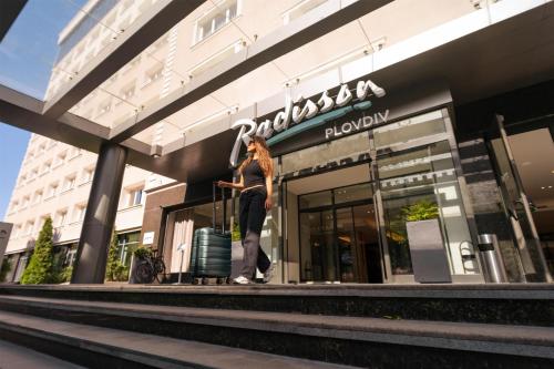 a woman standing in front of a store with a suitcase at Radisson Hotel Plovdiv in Plovdiv