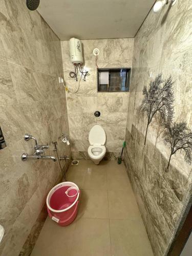 a bathroom with a toilet and a pink bucket at Rimzim's Tatvamasi - A Pool Villa Retreat in Kudāl