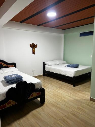 two beds in a room with a cross on the wall at Casa Hotel Villa María - Apia in Apía