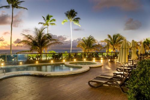 a resort pool with chairs and umbrellas and palm trees at Ritz Suites Grand Hotel Boutique in Maceió