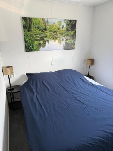 a bedroom with a blue bed with a painting on the wall at Luxe Chalet San Marco in Giethoorn