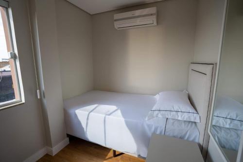 a small room with a white bed and a window at Ap de novela no centro da cidade com garagem in Toledo