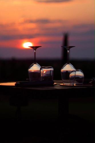 three glasses on a table with the sunset in the background at Casale Oliveta & Ristorante in Orbetello