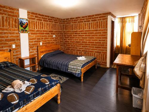 a bedroom with two beds and a brick wall at Hostal el Vaquero in Chugchilán