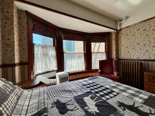 a bedroom with a bed and a chair and windows at Arundel Mansions Hotel in New Westminster