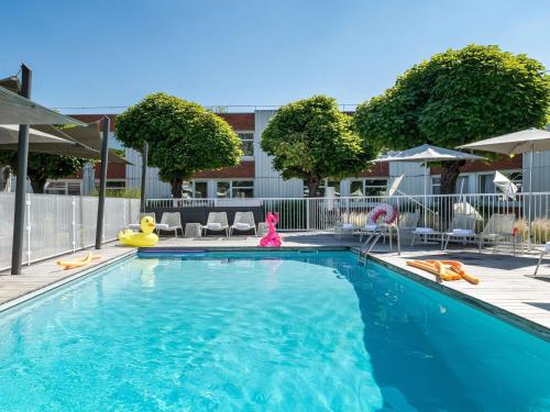 a swimming pool with chairs and umbrellas at ibis Styles Lyon Bron Eurexpo in Bron