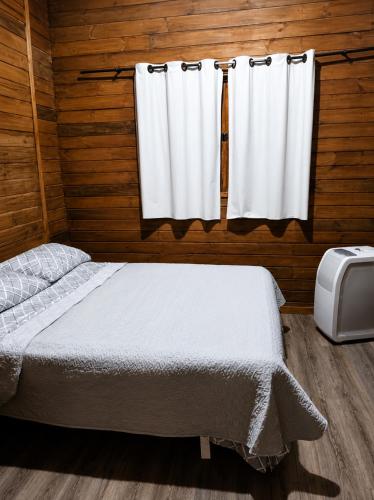a bedroom with a bed and two white curtains at Chalé Recanto da Cuesta in Botucatu