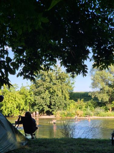 a person sitting in a chair next to a tent next to a river at Camping Bela krajina - Pitches in Gradac