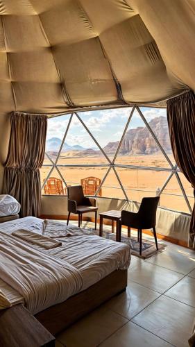 a bedroom with a bed and chairs and a large window at RUM PRESTIGE lUXURY CAMP & DESERT TOURS in Wadi Rum