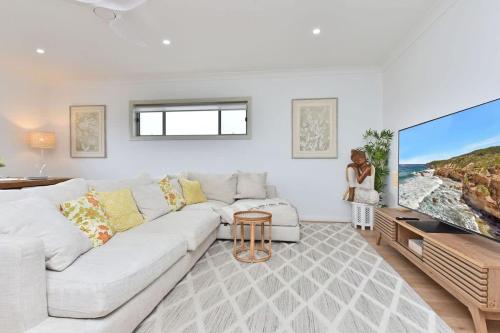 a living room with a white couch and a large tv at Finns at Caves Beach Resort in Caves Beach