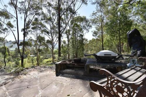 a bbq grill on a stone patio with a bench at Corymbia Cottage Brokes Secluded Escape for max 4 in Broke