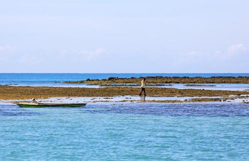 a man standing on the beach with a boat in the water at Pousada Lua Cheia in Japaratinga
