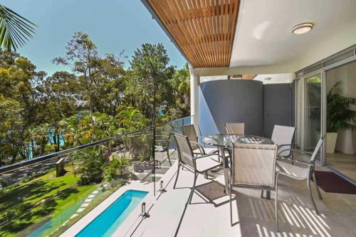 a balcony with a table and chairs and a swimming pool at Park Cove Apartments in Noosa Heads